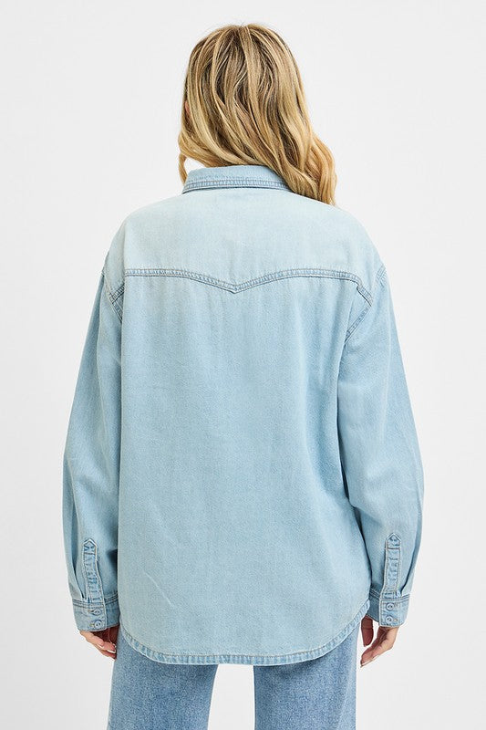 Woman wearing a light blue denim jacket and jeans on a plain background