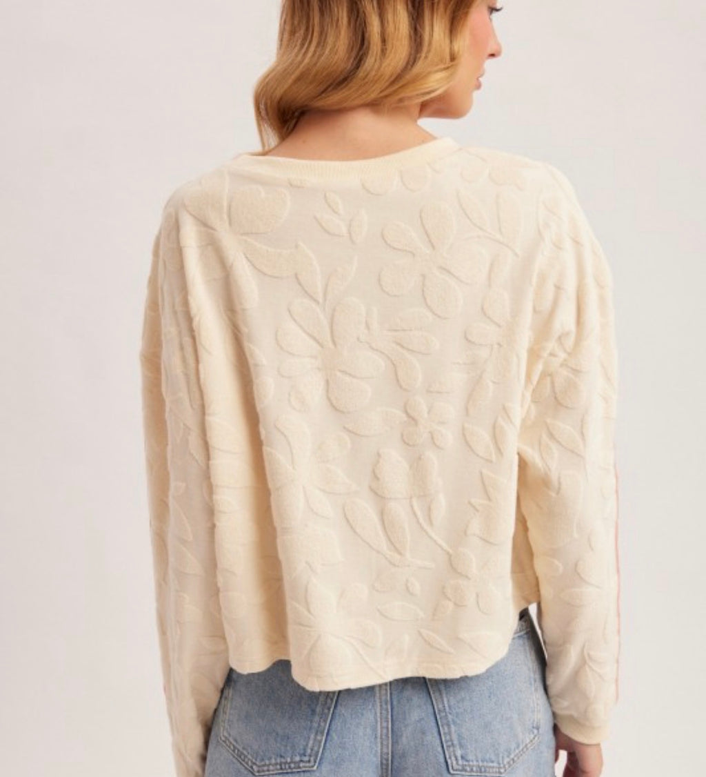 Woman wearing a beige Embossed knit sweater with pink stripes on a plain background