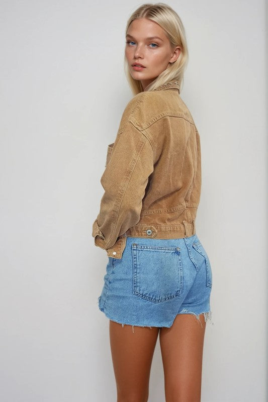 Woman wearing a tan denim jacket and blue shorts on a white background