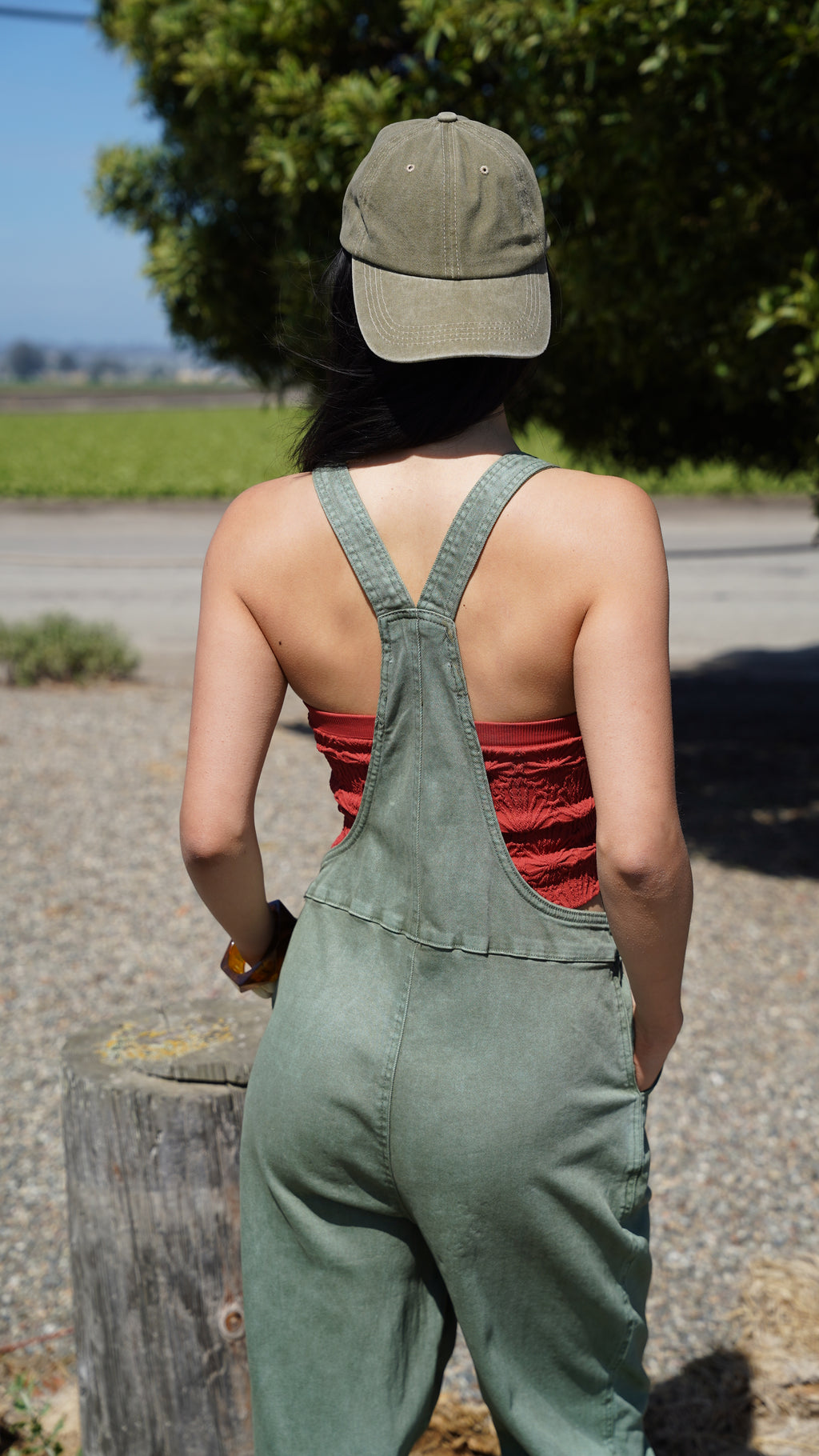 Person wearing green overalls standing outdoors with trees and a path in the background