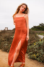 Woman in a rust-colored dress standing outdoors with greenery in the background