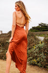 Woman in a rust-colored dress standing outdoors with greenery in the background