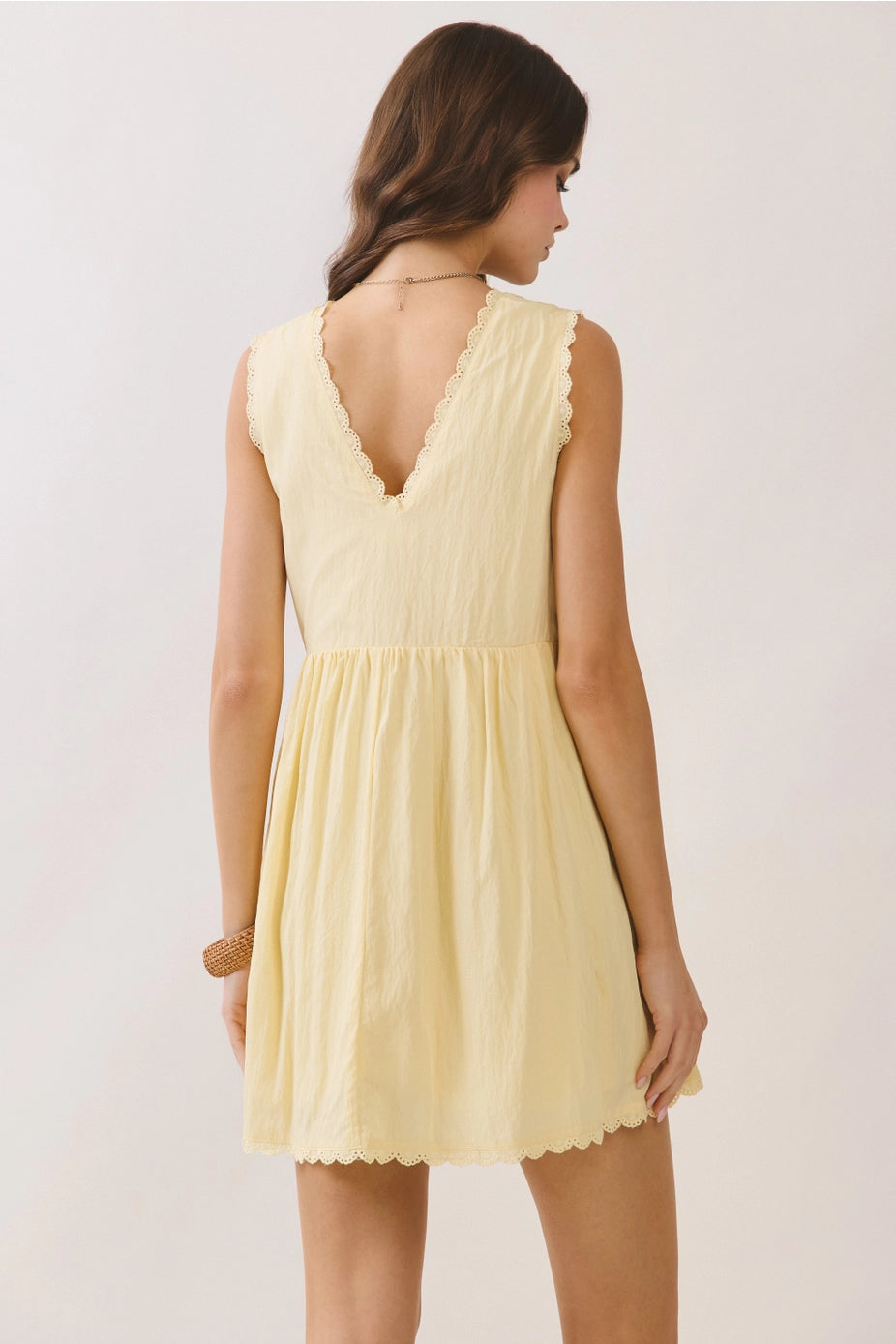 Woman wearing a yellow dress with lace details on a plain background