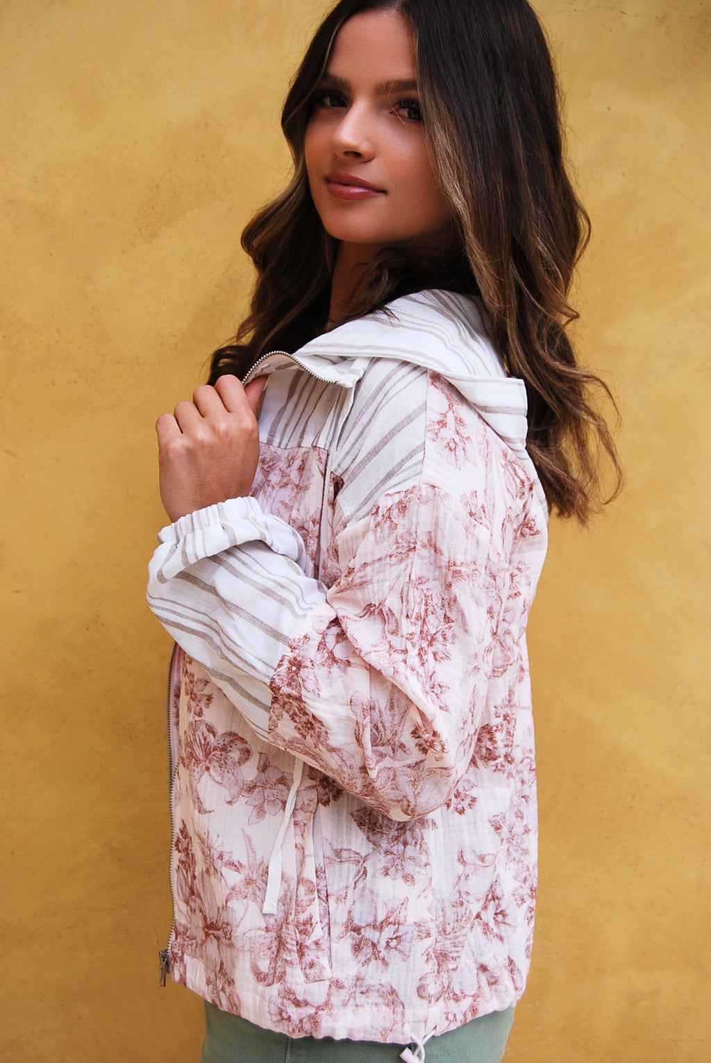 Woman wearing a floral jacket over a pink top and green shorts against a yellow wall