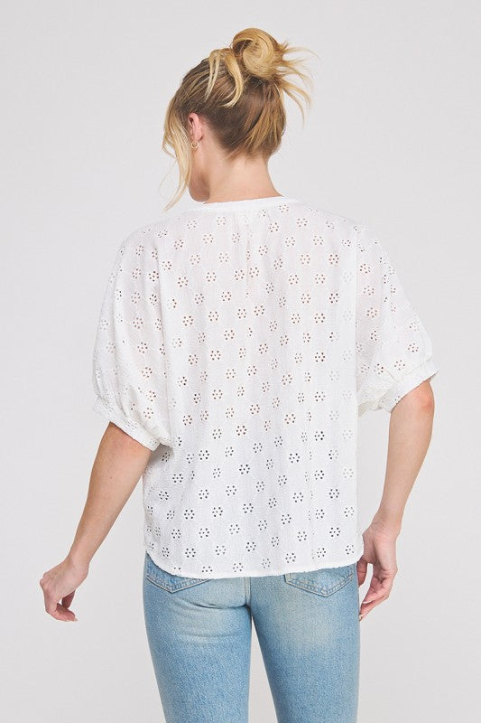 Woman wearing a white eyelet blouse and blue jeans on a plain background