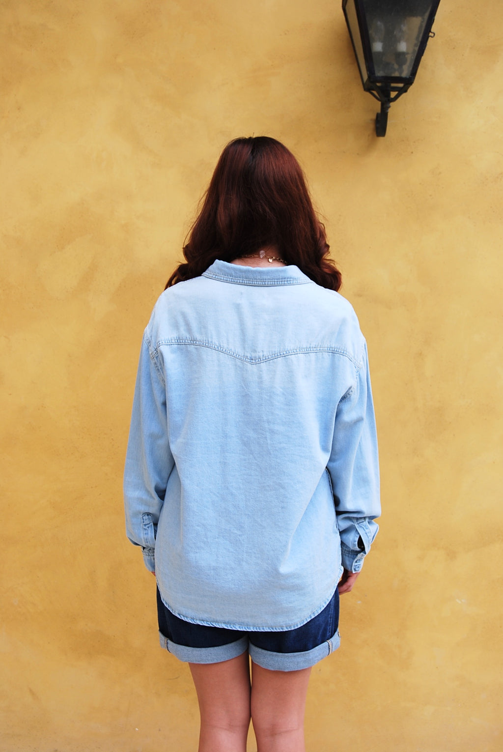 Woman wearing a denim jacket and headscarf in front of greenery