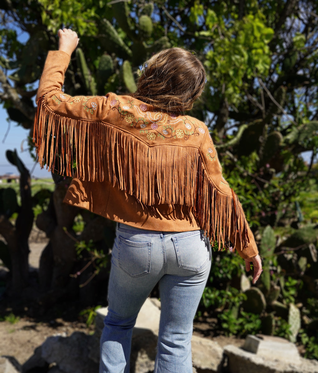 Person wearing a brown suede jacket with fringe and embroidery, blue top, and jeans.