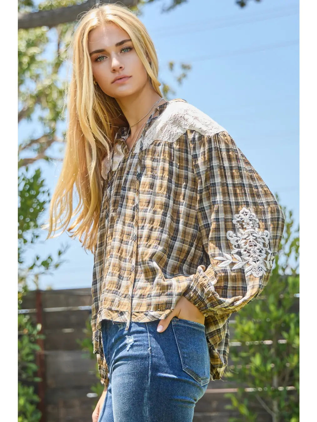 Woman wearing a plaid shirt, jeans, and a cap with 'Harvest' on it, standing outdoors.