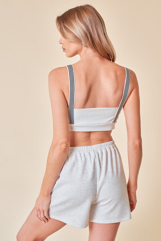 Woman wearing a white crop top and shorts with button details on a beige background