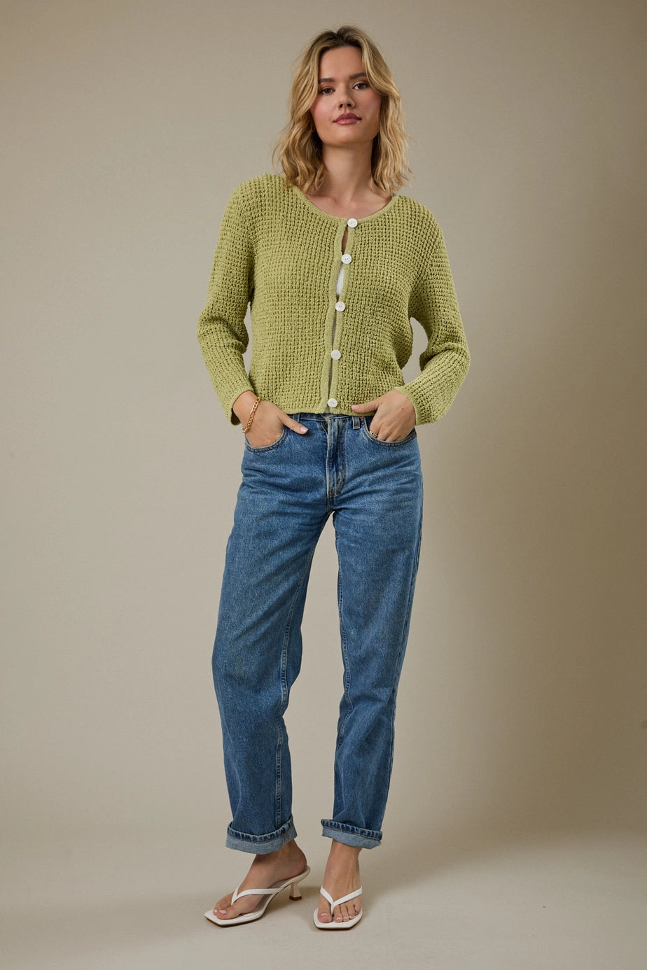 Woman wearing a green knitted cardigan with a beige background