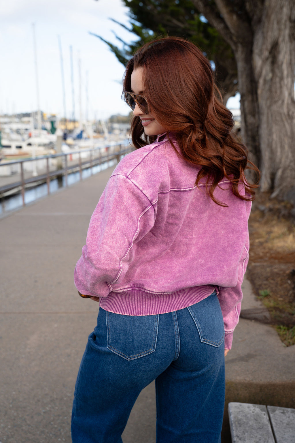 Woman wearing a pink jacket and sunglasses by a marina