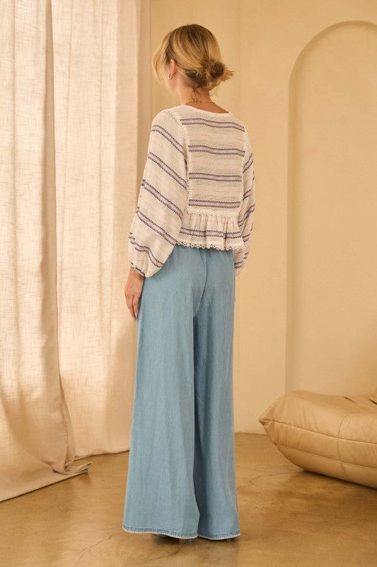 Woman wearing a striped top and light blue pants against a beige background