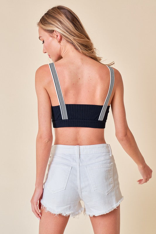 Woman wearing a black ribbed crop top and white pants against a beige background