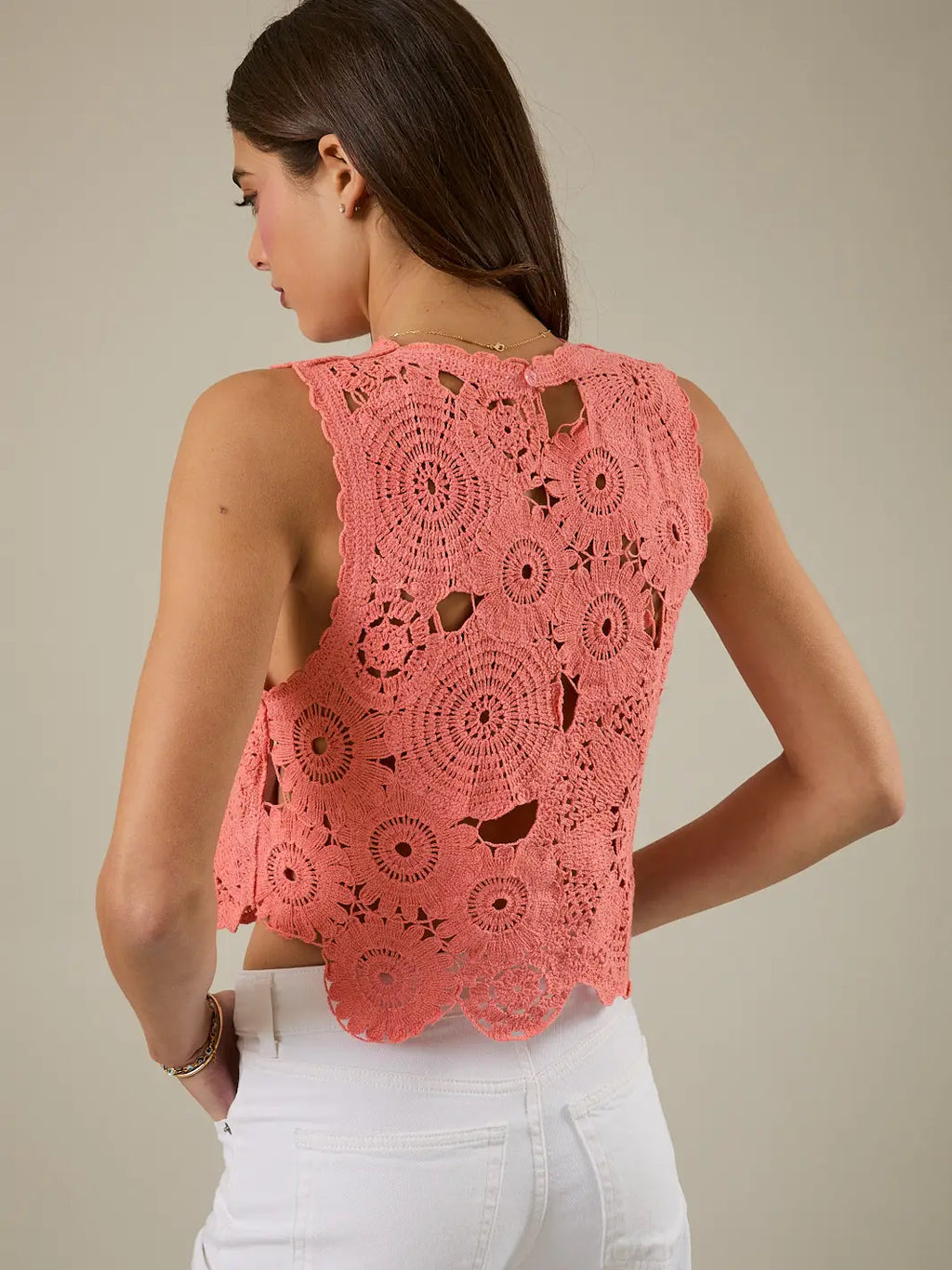 Woman wearing a coral lace top and white pants against a beige background