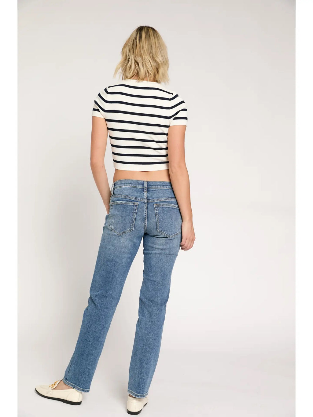 Woman wearing a black and white striped shirt and blue jeans on a plain background