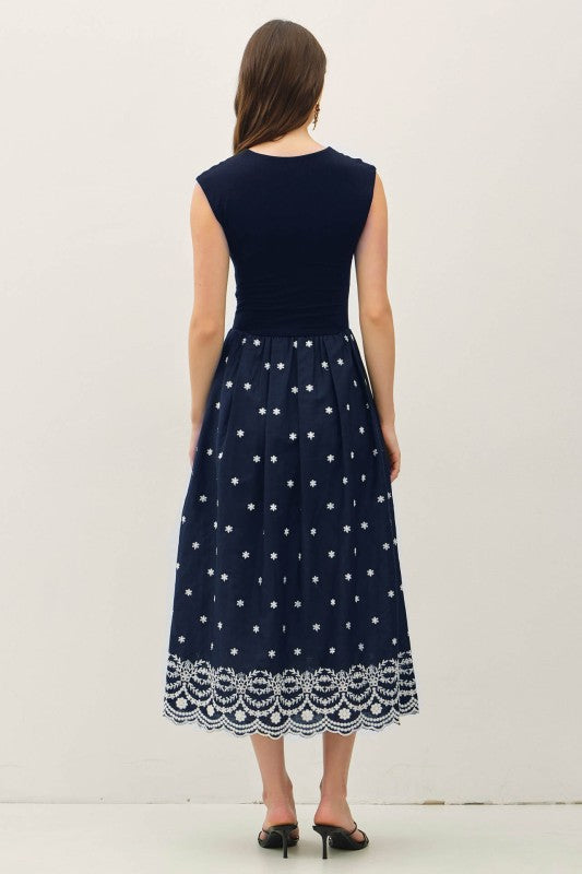 Woman wearing a navy blue dress with white star patterns and lace hem on a light gray background