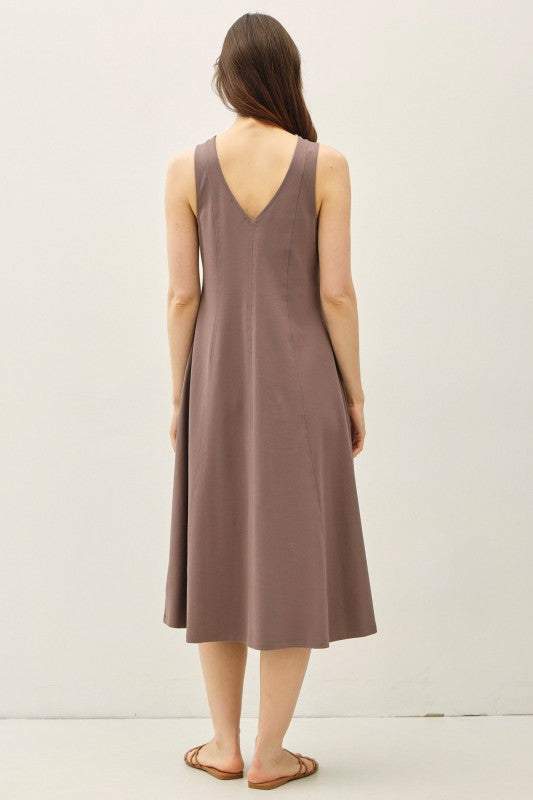 Woman wearing a sleeveless brown dress against a plain background