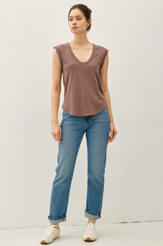 Woman wearing a brown sleeveless top and blue jeans against a plain background