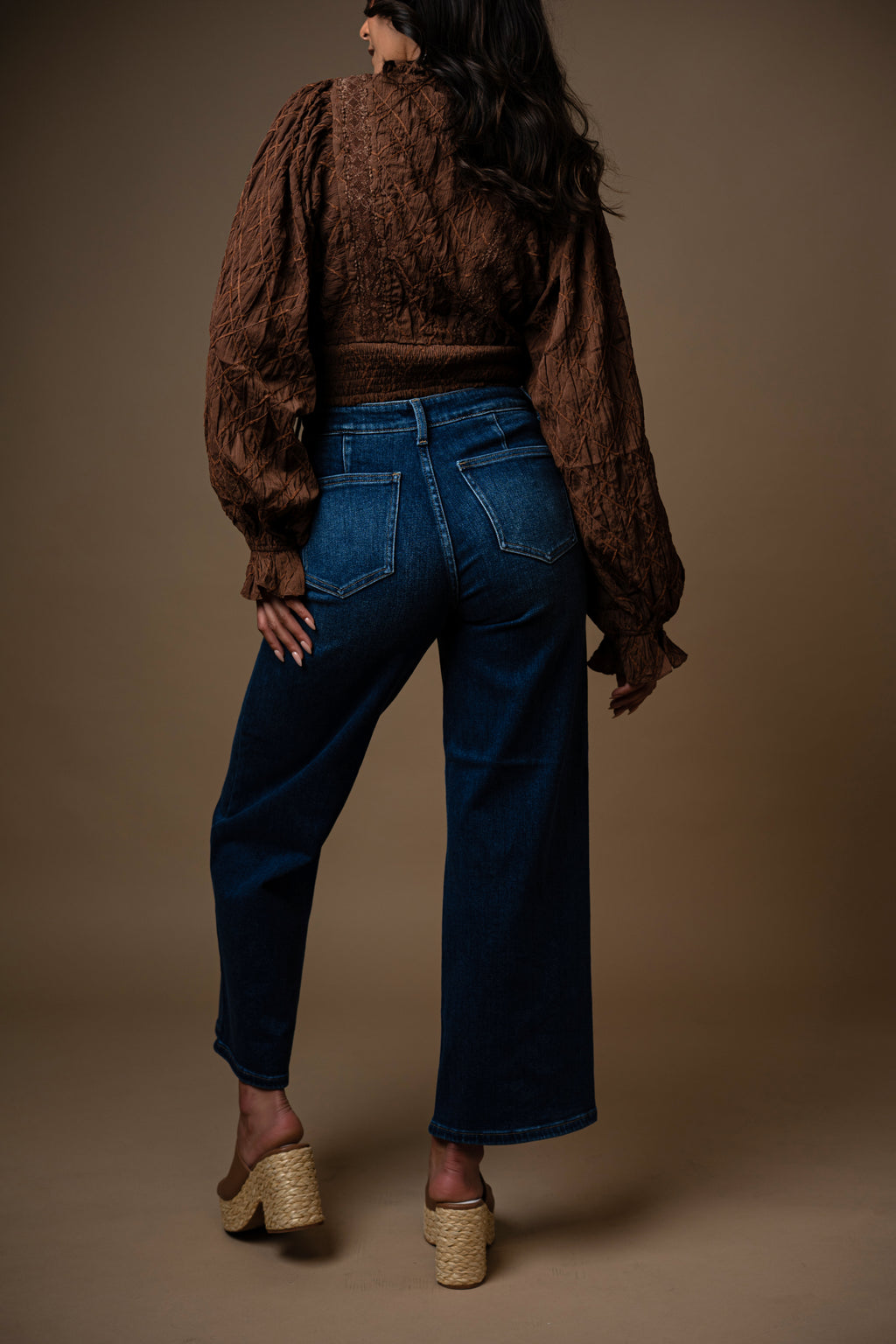 Woman wearing a brown shirt and blue jeans against a brown background