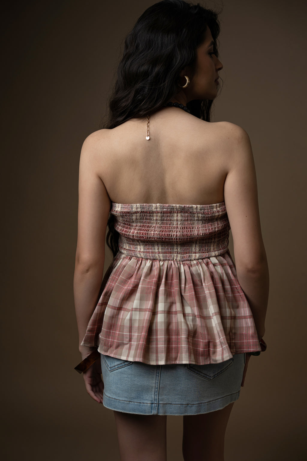 Woman wearing a plaid top and denim skirt against a brown background