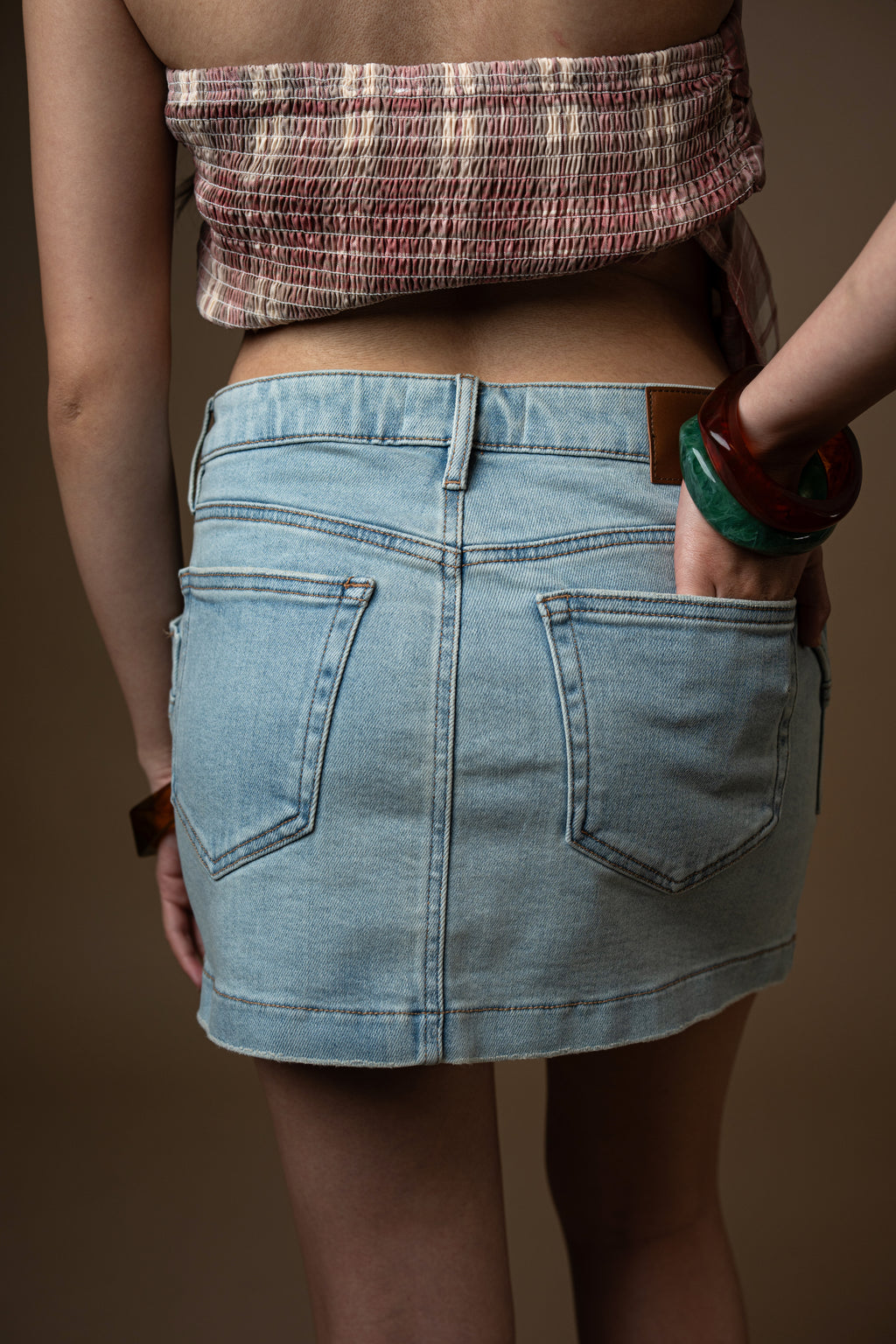 Person wearing a light blue denim skirt against a brown background