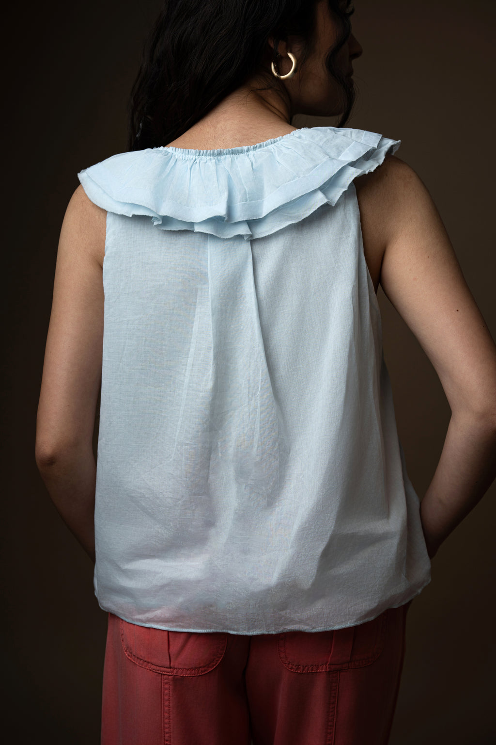 Woman wearing a light blue ruffled top and Coral pants against a brown background