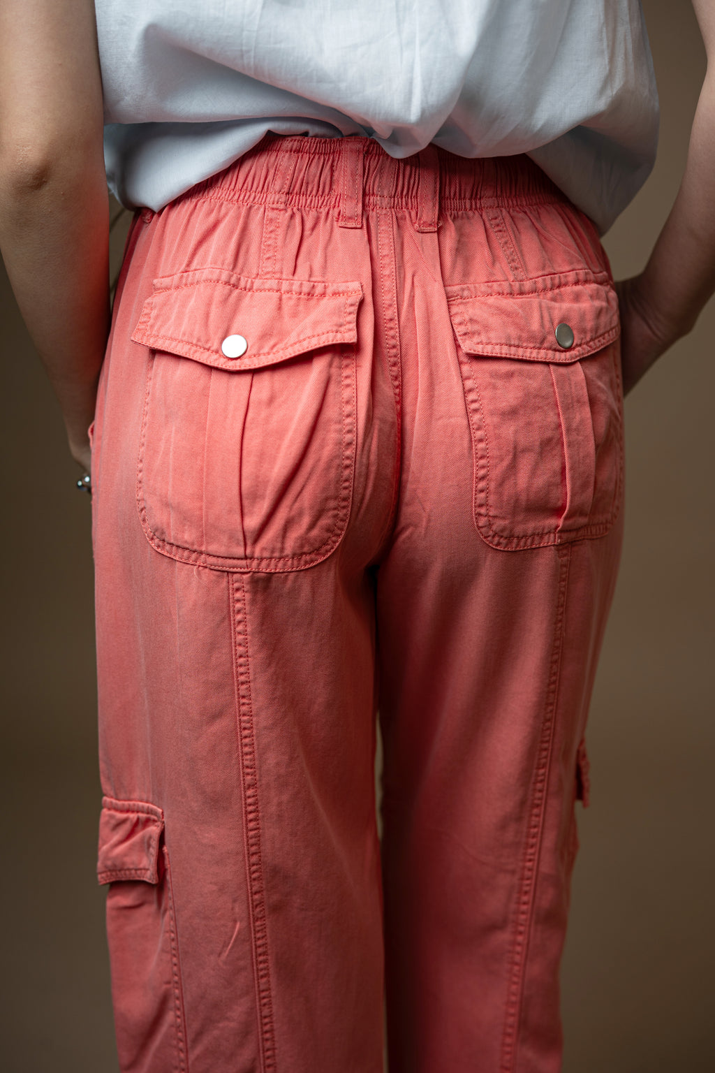 Person wearing coral cargo pants on a brown background