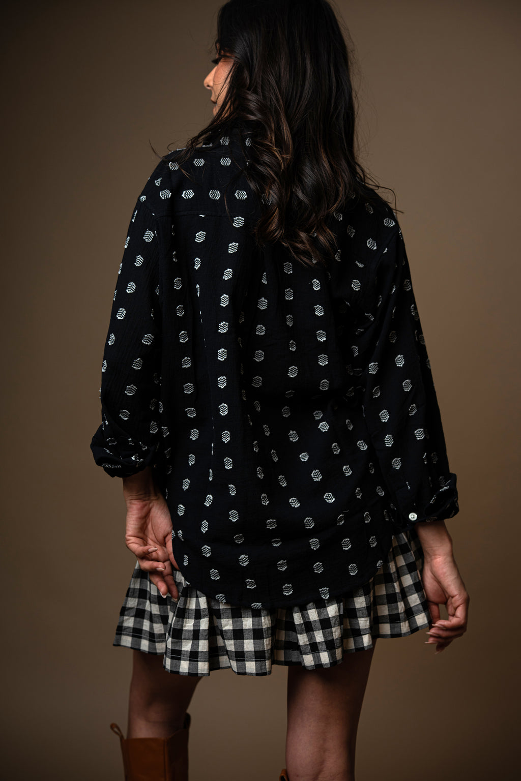 Person wearing a black patterned top and plaid skirt against a brown background