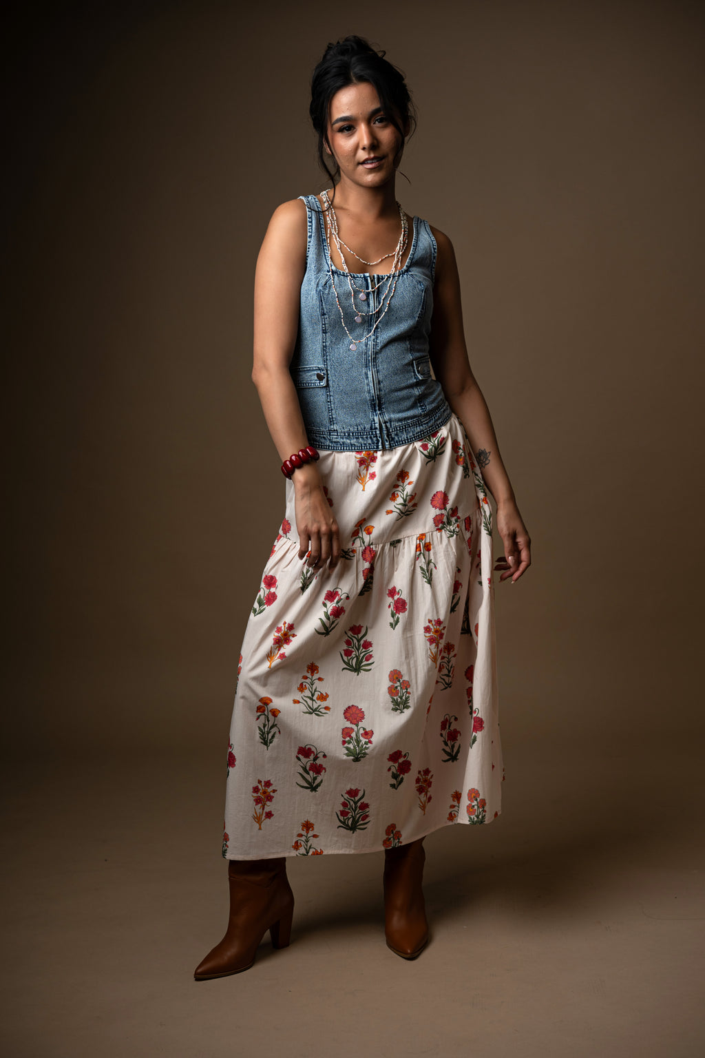 Person wearing a denim top and floral skirt on a brown background