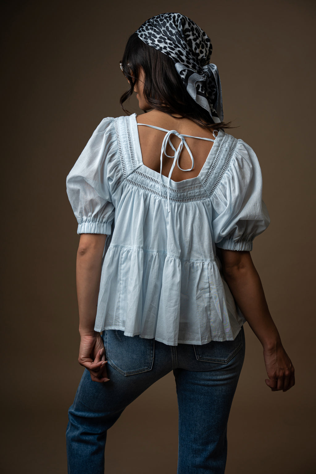 Woman wearing a light blue blouse with puff sleeves against a brown background