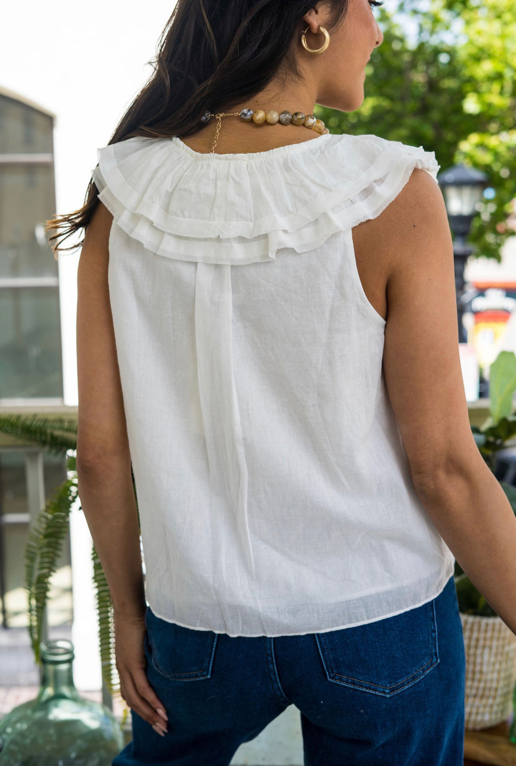 Woman wearing a white blouse with lace details and blue jeans outdoors.