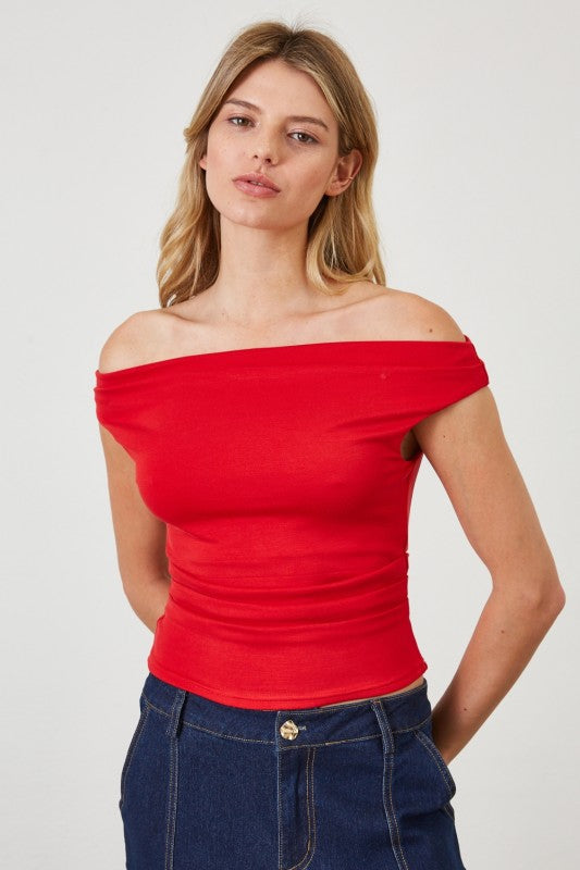 Woman wearing a red off-shoulder top and blue jeans against a white background