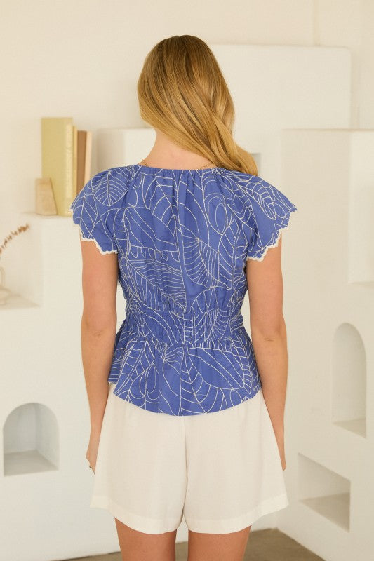 Woman wearing a blue patterned top and white shorts in a bright room.