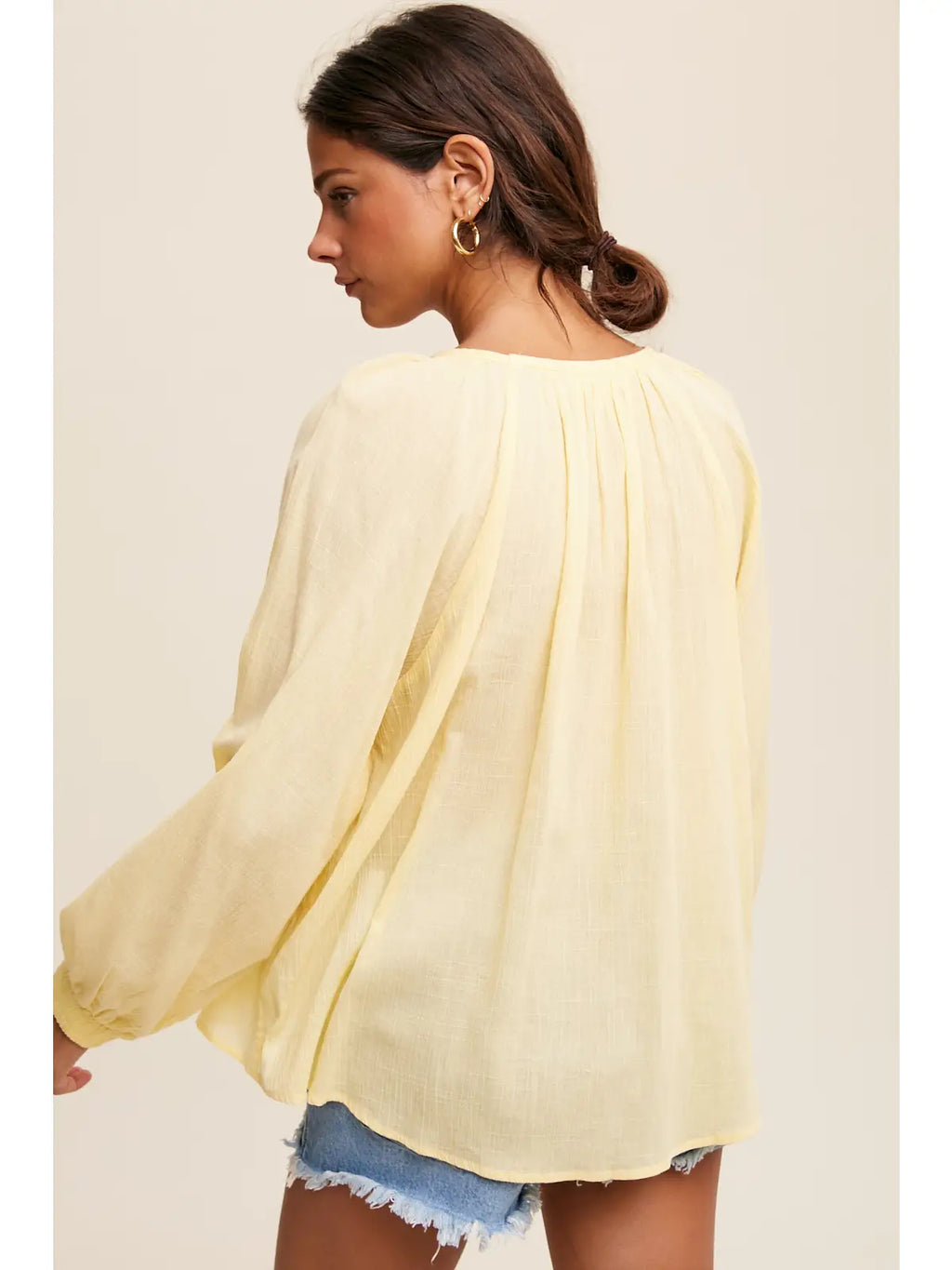 Woman wearing a light yellow blouse with lace-up front on a plain background