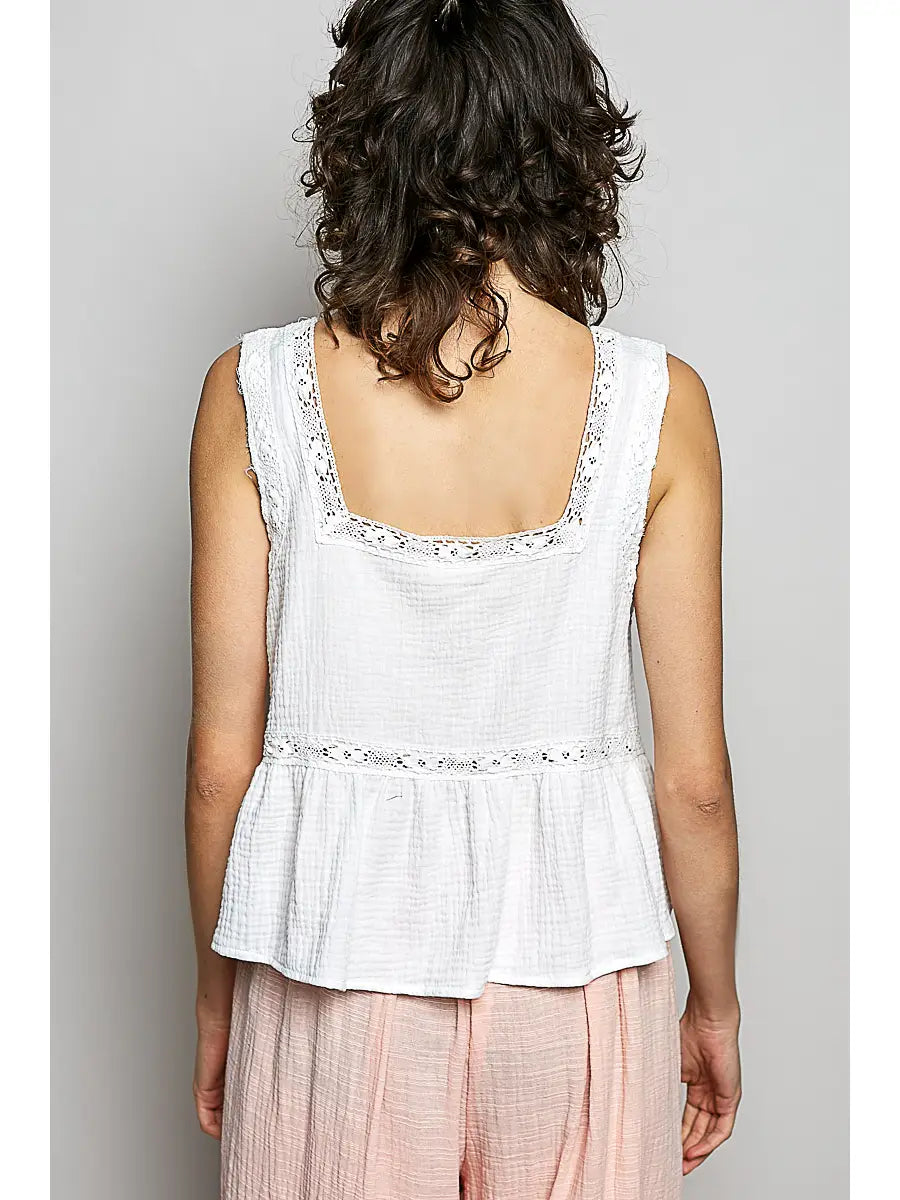 Woman wearing a white sleeveless top with floral embroidery on a plain background