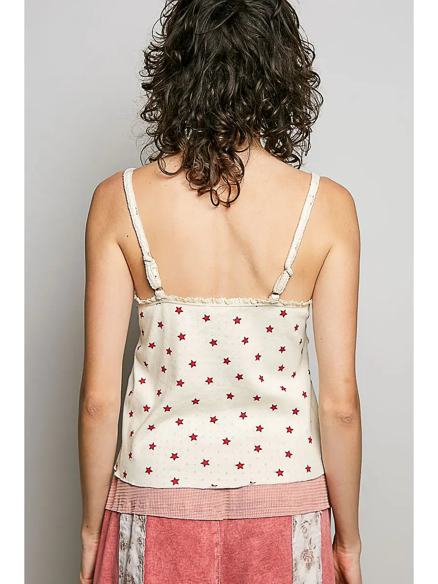 Woman wearing a white tank top with red star patterns and pink pants against a plain background