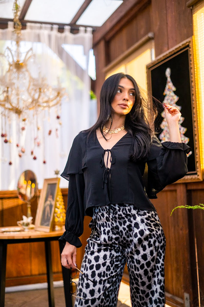 Woman in black top and leopard print pants standing in a decorated room with chandelier and Christmas tree.